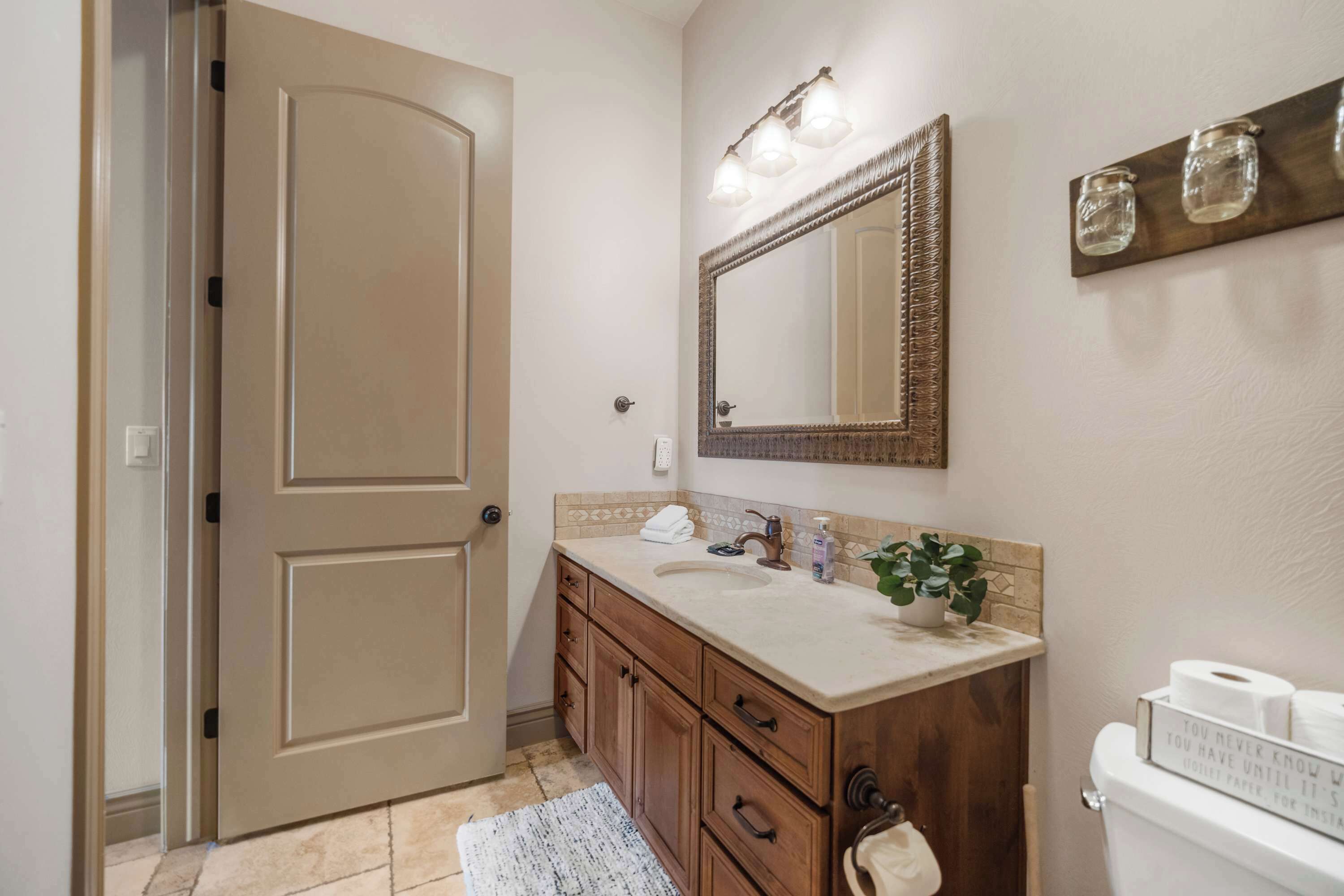 A bathroom with a beige door, a vanity with a mirror, a sink, and a toilet.