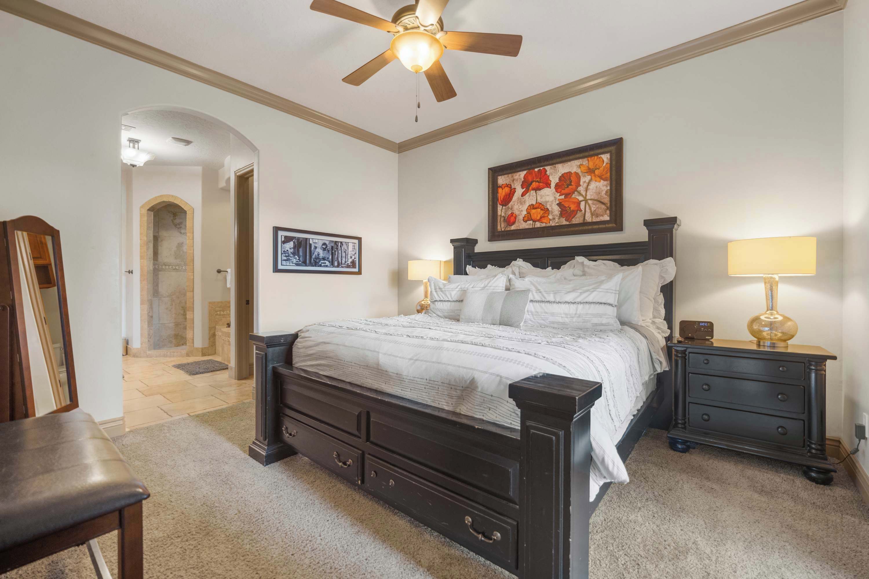 A bedroom with a dark wooden bed, two bedside tables with lamps, a ceiling fan, and a framed picture on the wall.