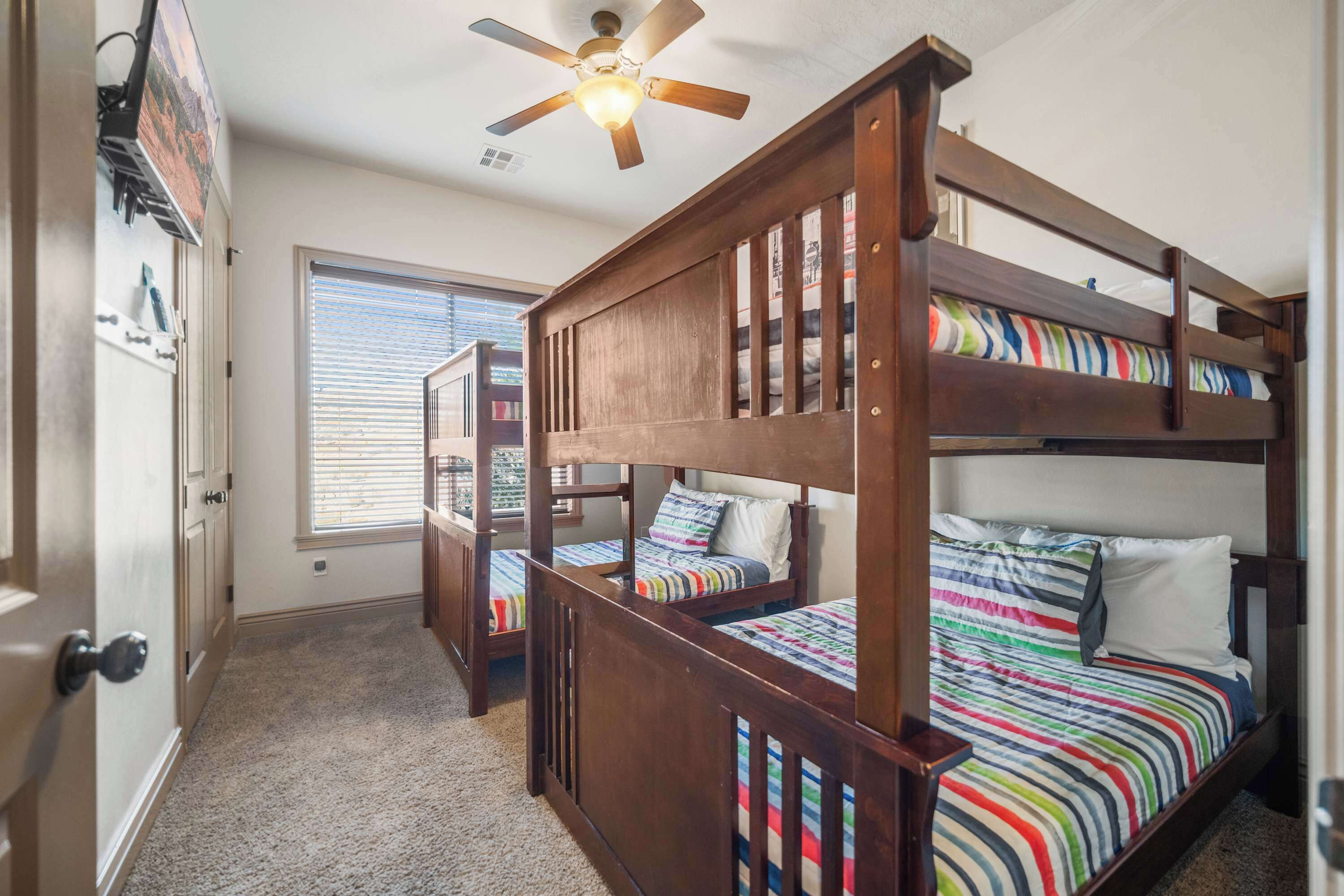 A room with bunk beds, a ceiling fan, a window with blinds, and a door with a handle.