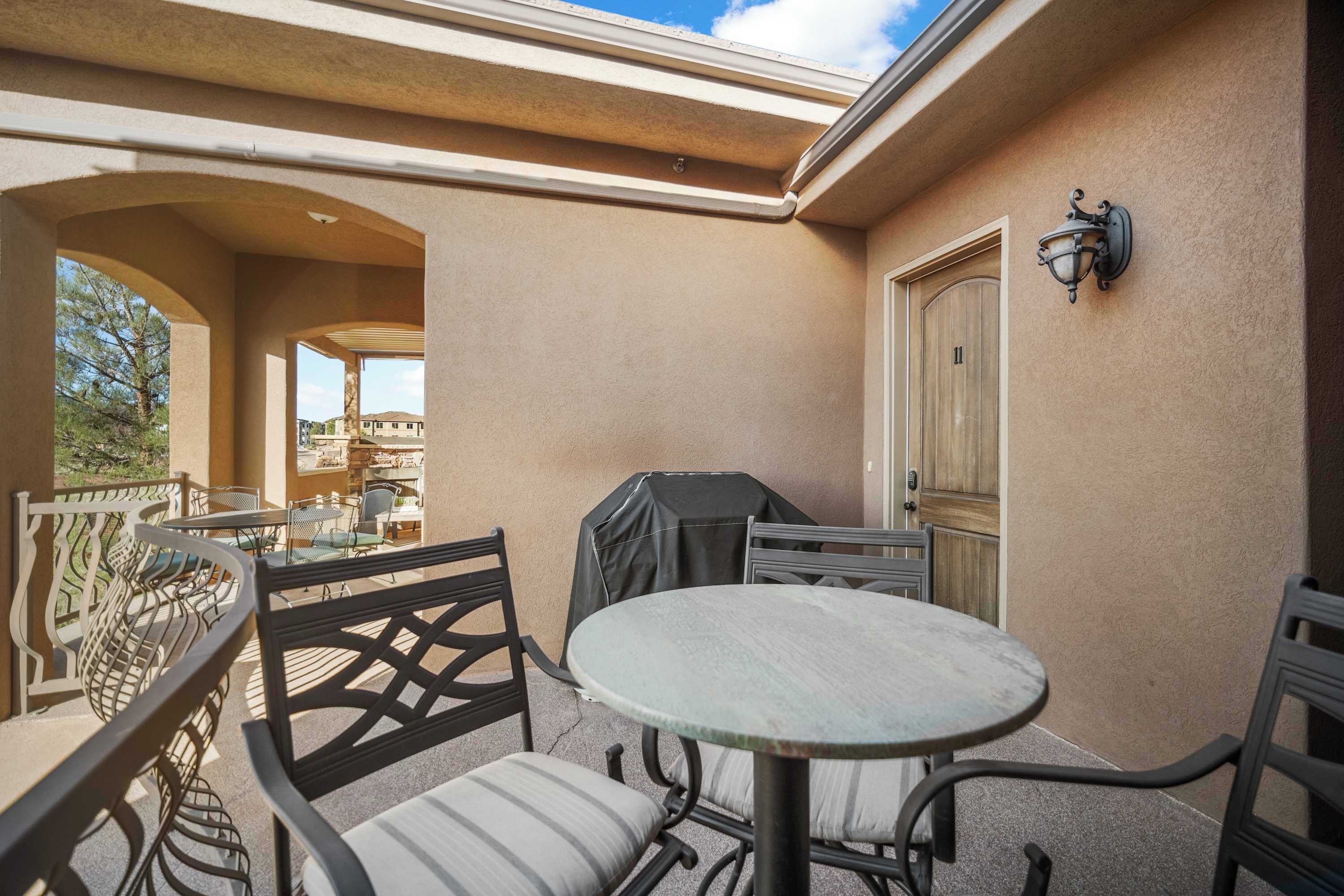 An outdoor patio with a round table and chairs, a covered grill, and a door.