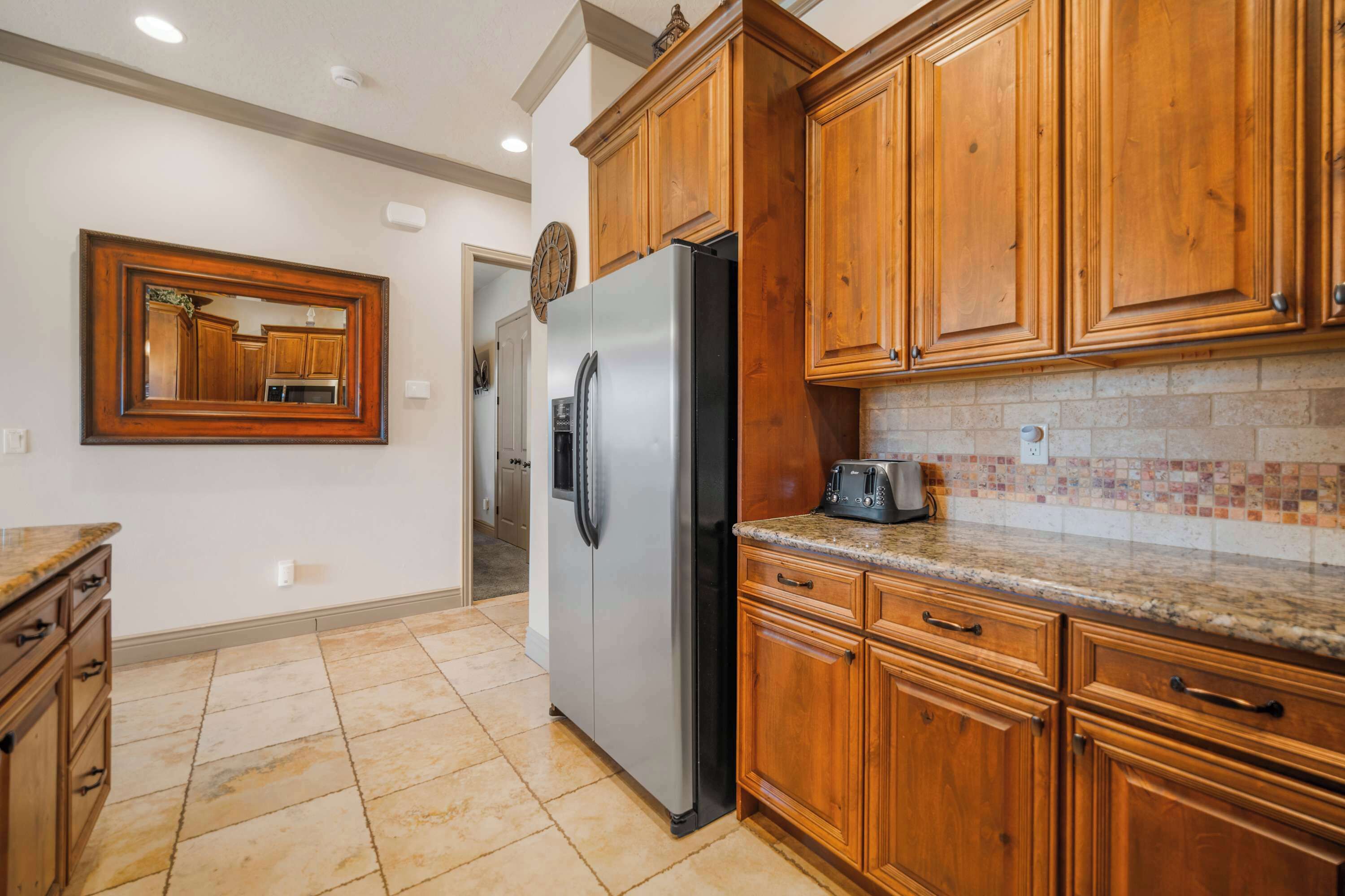 Una cocina con gabinetes de madera, un refrigerador de acero inoxidable, un salpicadero de azulejos y una encimera de granito.