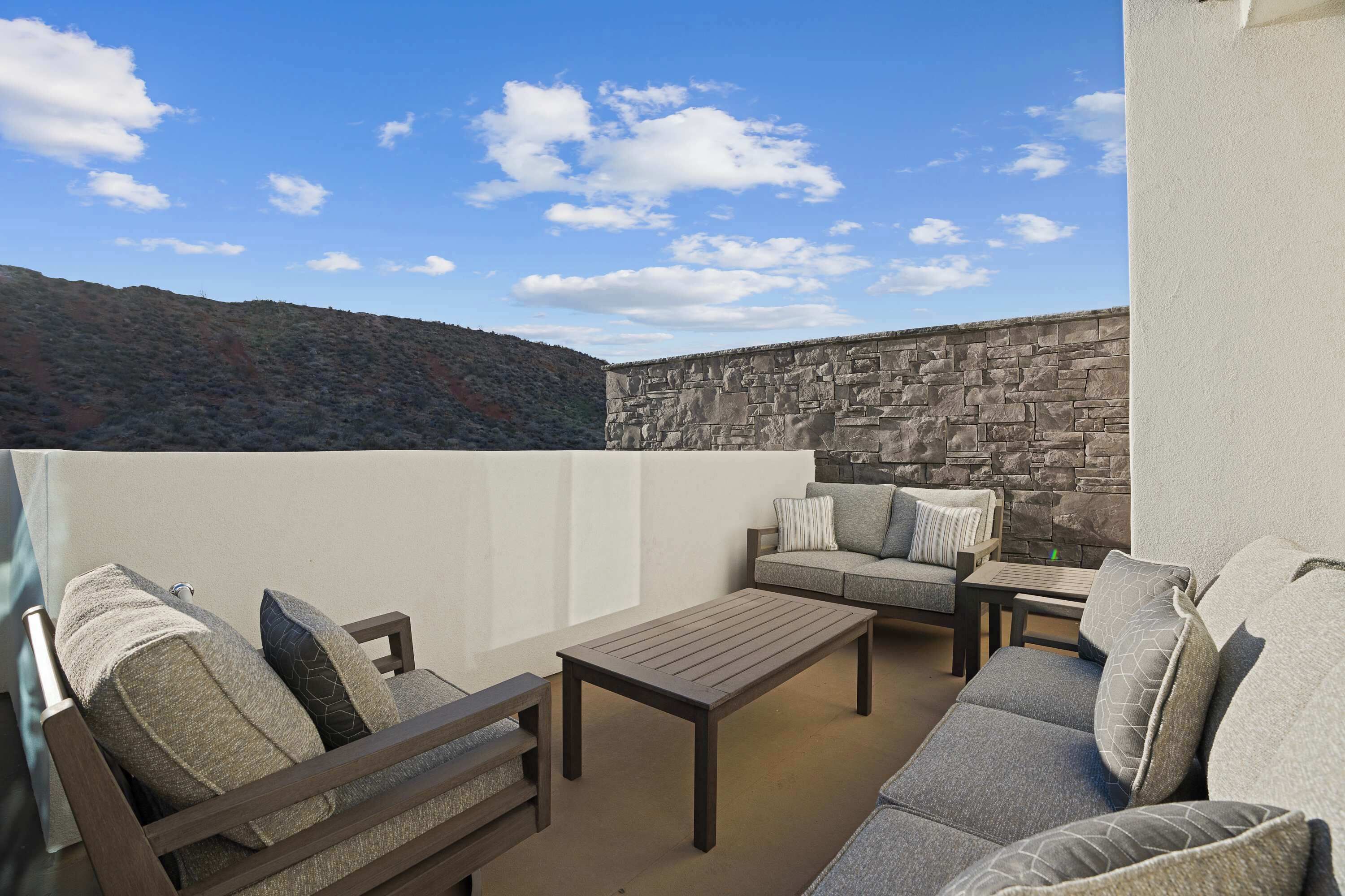 Eine Dachterrasse mit einer Steinmauer, einem Holztisch und zwei Sofas mit Kissen.