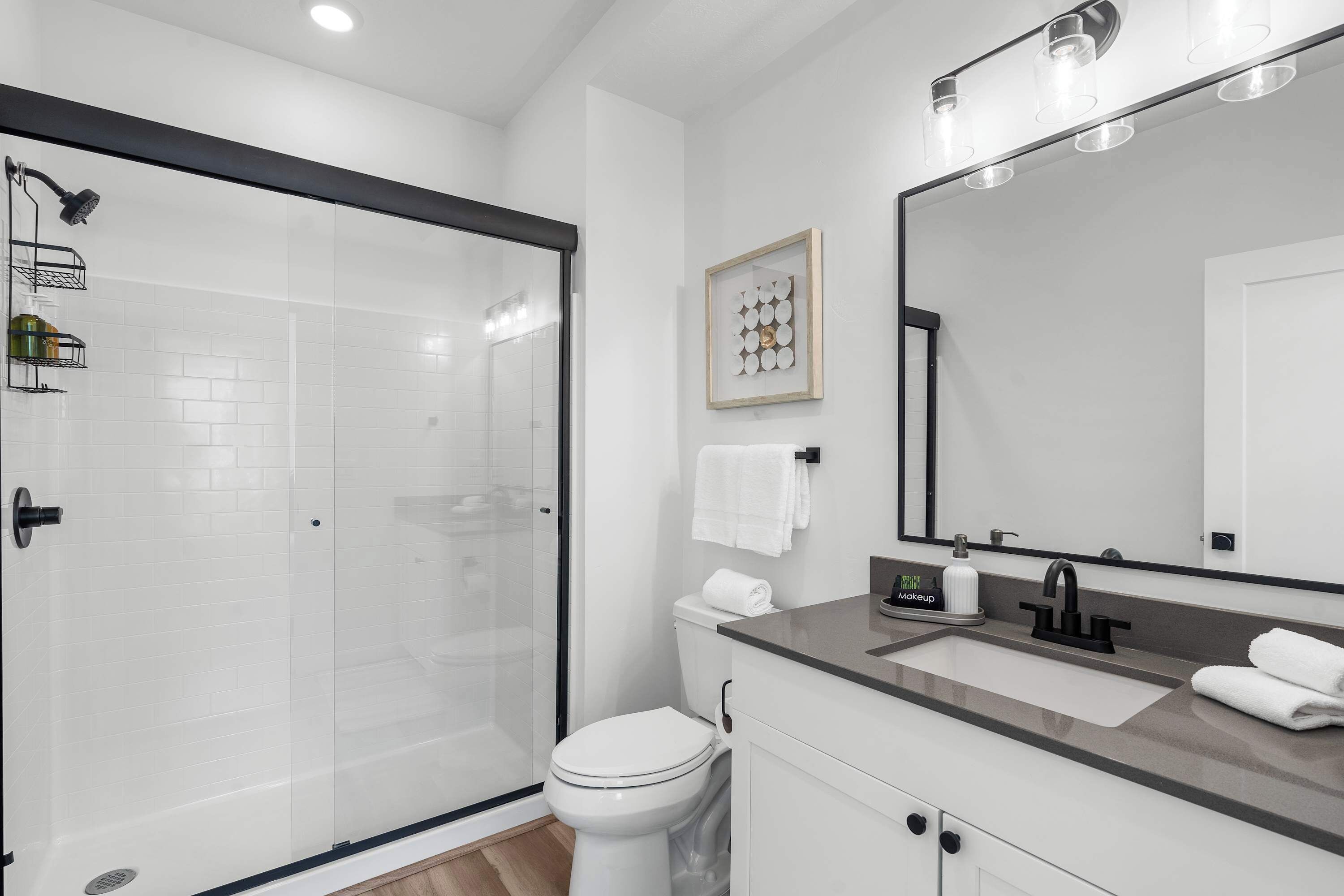 Un baño moderno con ducha de vidrio, inodoro blanco, lavamanos con espejo y una obra de arte enmarcada en la pared.