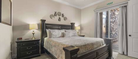 A bedroom with a bed, nightstands, lamps, a ceiling fan, and an exit sign.