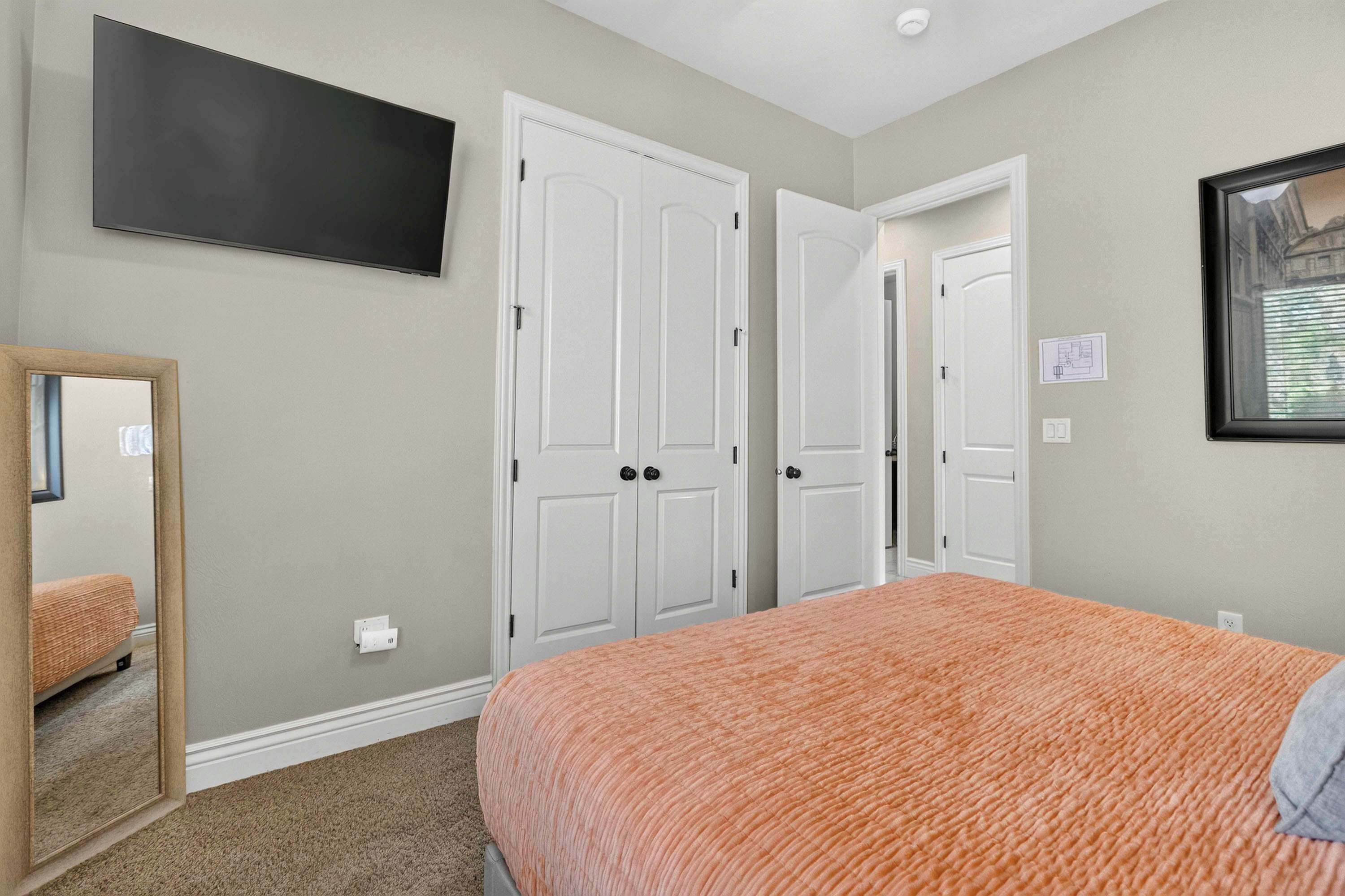 Un dormitorio con una cama, un televisor instalado en la pared y una puerta que da a otra habitación.