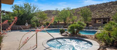 A pool area with a hot tub, surrounded by desert vegetation and a mountain backdrop.