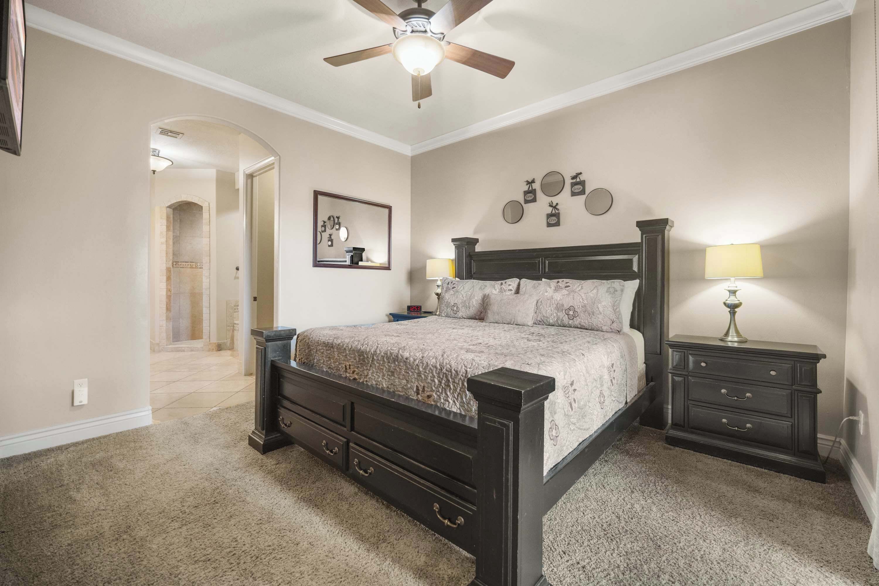 A bedroom with a bed, nightstands, a ceiling fan, and a hallway leading to another room.