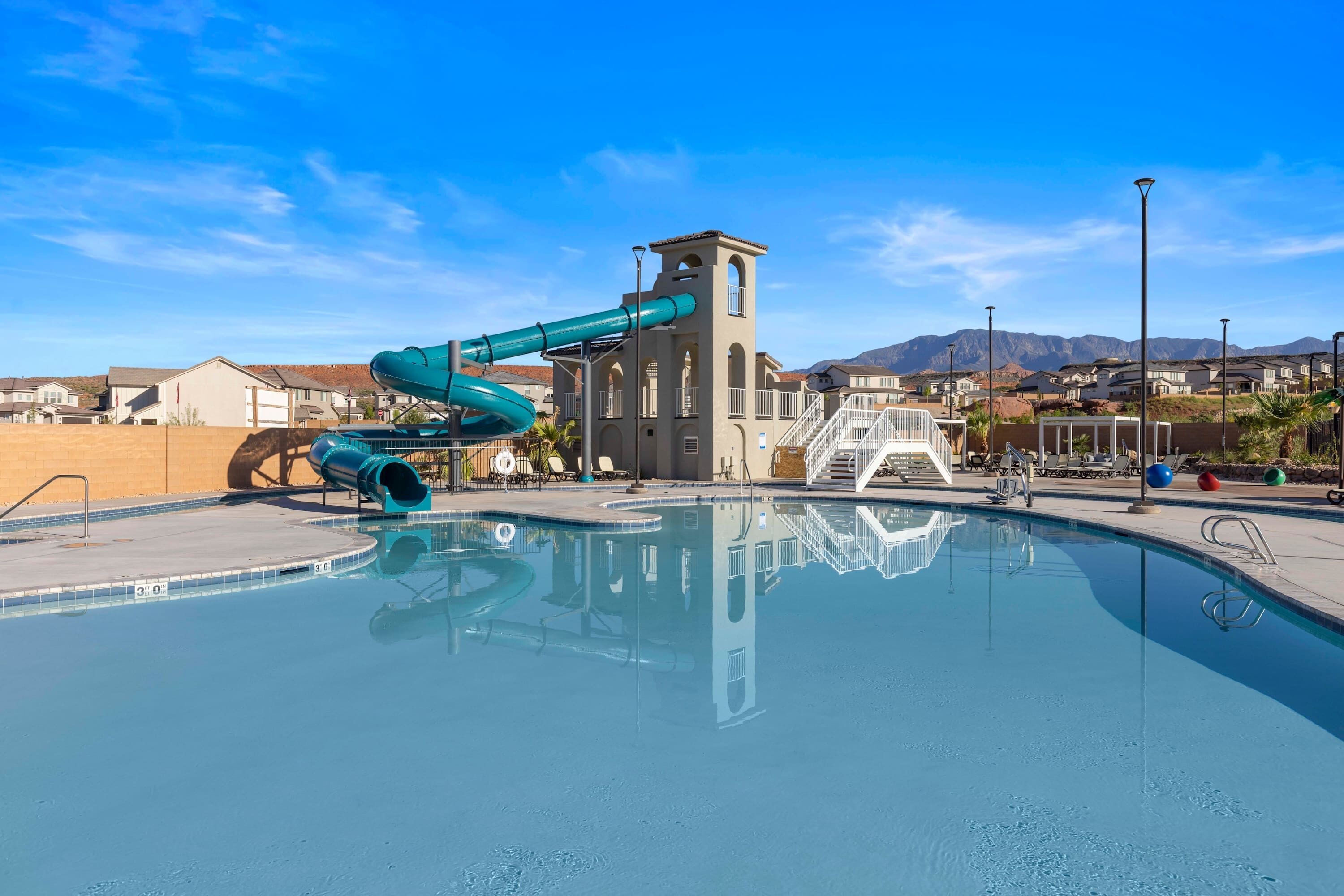 A swimming pool with a water slide, a tower structure, and a view of houses and mountains in the background.