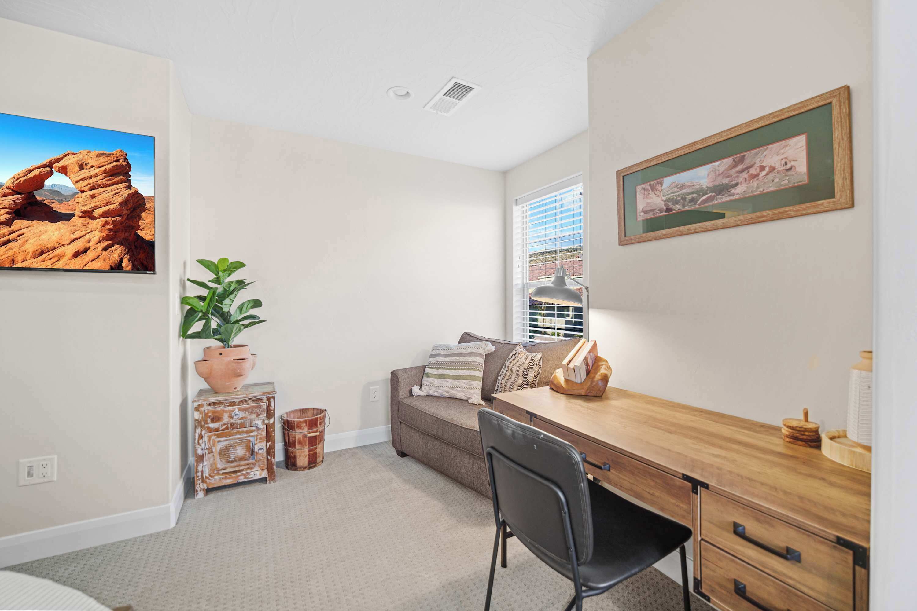 A room with a wooden desk, a brown sofa, a potted plant, and a framed picture on the wall.
