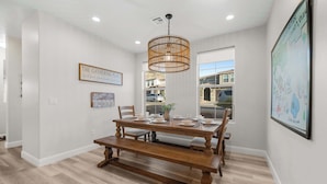 Un coin repas avec une table en bois dressée pour quatre personnes, un luminaire suspendu et une carte accrochée au mur.