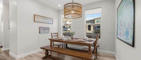 A dining area with a wooden table set for four, a hanging light fixture, and a map on the wall.