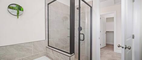Een moderne badkamer met een douche met glazen wand, een witte badkuip en een aan de muur bevestigde plant.