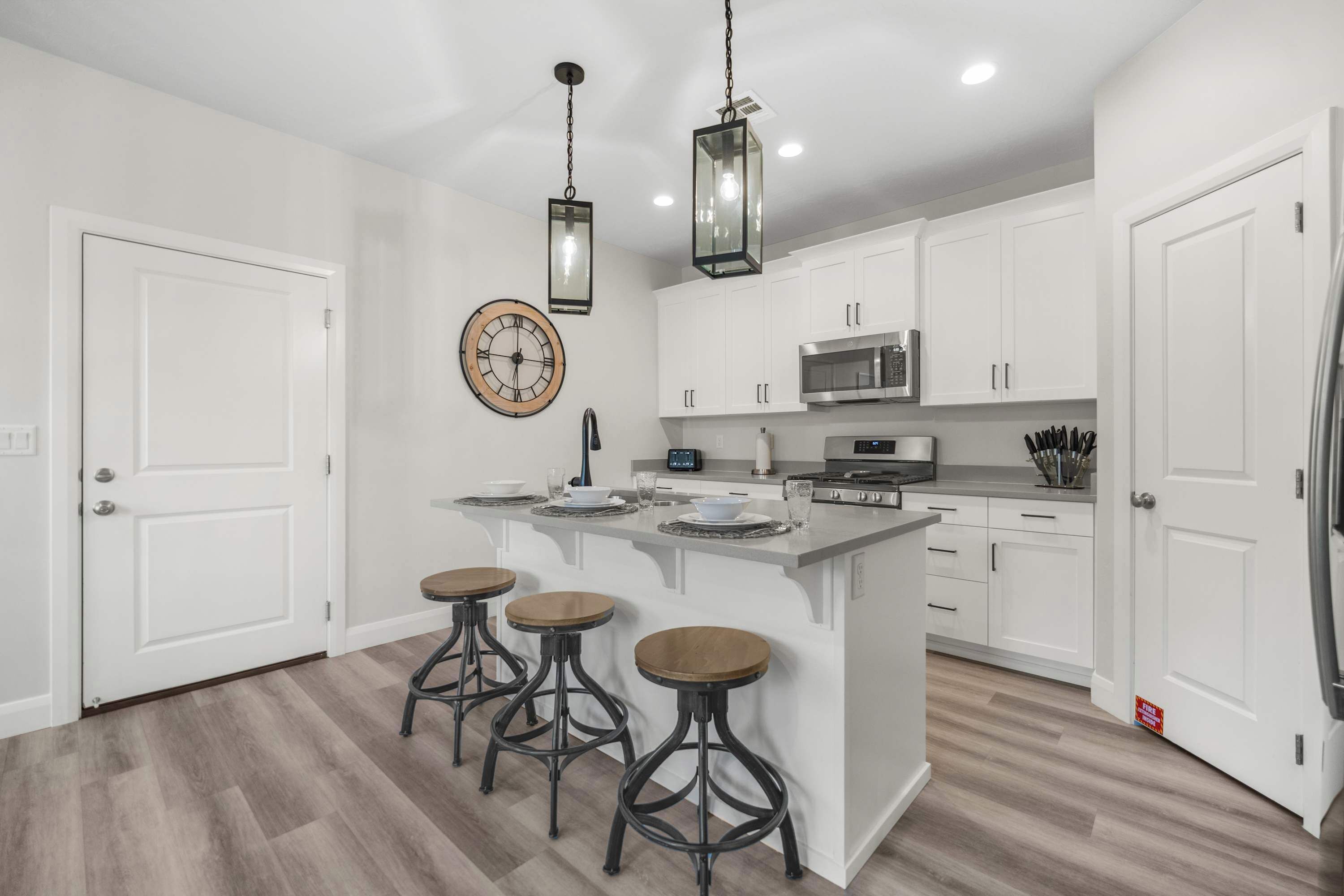 A modern kitchen with white cabinets, a central island with stools, stainless steel appliances, and pendant lighting.