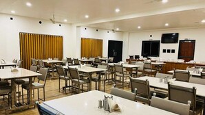 A spacious dining area with multiple tables and chairs, ceiling fans, and a television screen on the wall. - Gokul Resort  (Talala)