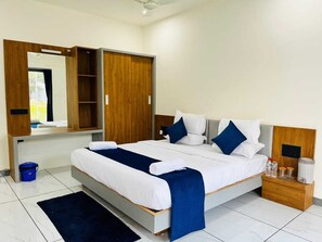 A modern hotel room with a large bed, a wooden wardrobe, a bedside table with a lamp, and a small blue rug. - Gokul Resort (Talala)