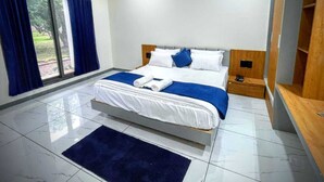 A modern hotel room with a large bed, a wooden headboard, a small bedside table, and a built-in wardrobe. - Gokul Resort  (Talala)