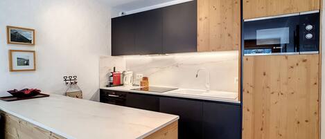Une cuisine moderne avec un îlot central en bois, des meubles de rangement noirs et un four à micro-ondes de la marque Bosch.