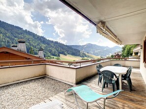En balkon med bord og stole, der giver udsigt over et bjerglandskab.