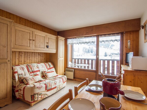 L’intérieur chaleureux d’un chalet avec un canapé en bois, une table à manger, des chaises et une fenêtre donnant sur un paysage enneigé.