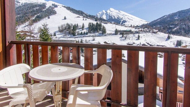 Ein Holzbalkon mit Tisch und zwei Stühlen mit Blick auf eine verschneite Berglandschaft.