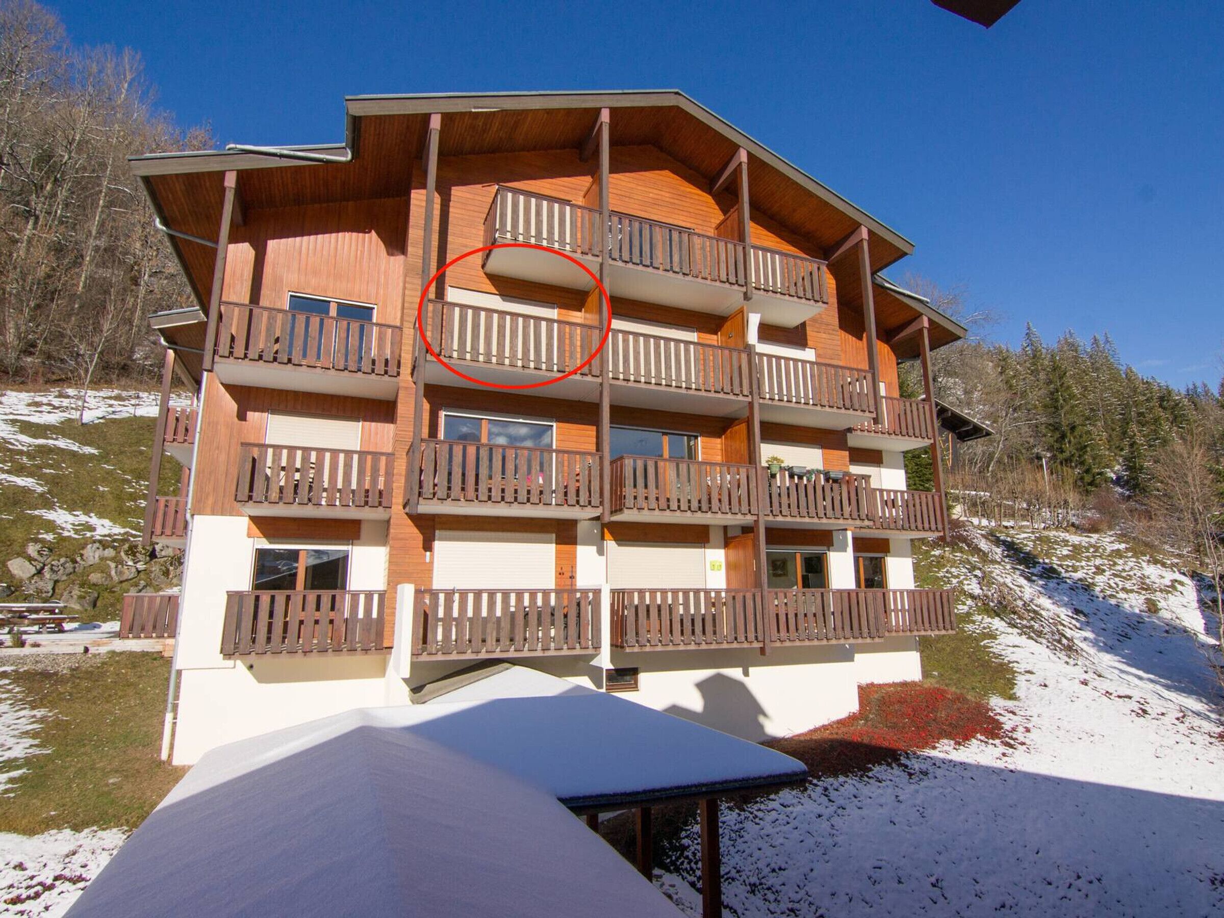 A multi-story building with wooden balconies, a ski slope in the background, and a snow-covered ground.