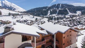 Ein verschneites Bergstädtchen mit Holzhäusern und einer Skipiste im Hintergrund.