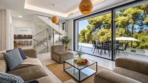 A modern living room with a glass coffee table, sofas, and a view of a dining area and trees. - Villas Pinares de San Antón, Saltwater pool, Sea, City, Mountain Views (Málaga)