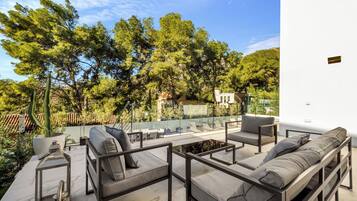 Un espacio al aire libre con mobiliario moderno, rodeado de árboles y un edificio blanco.