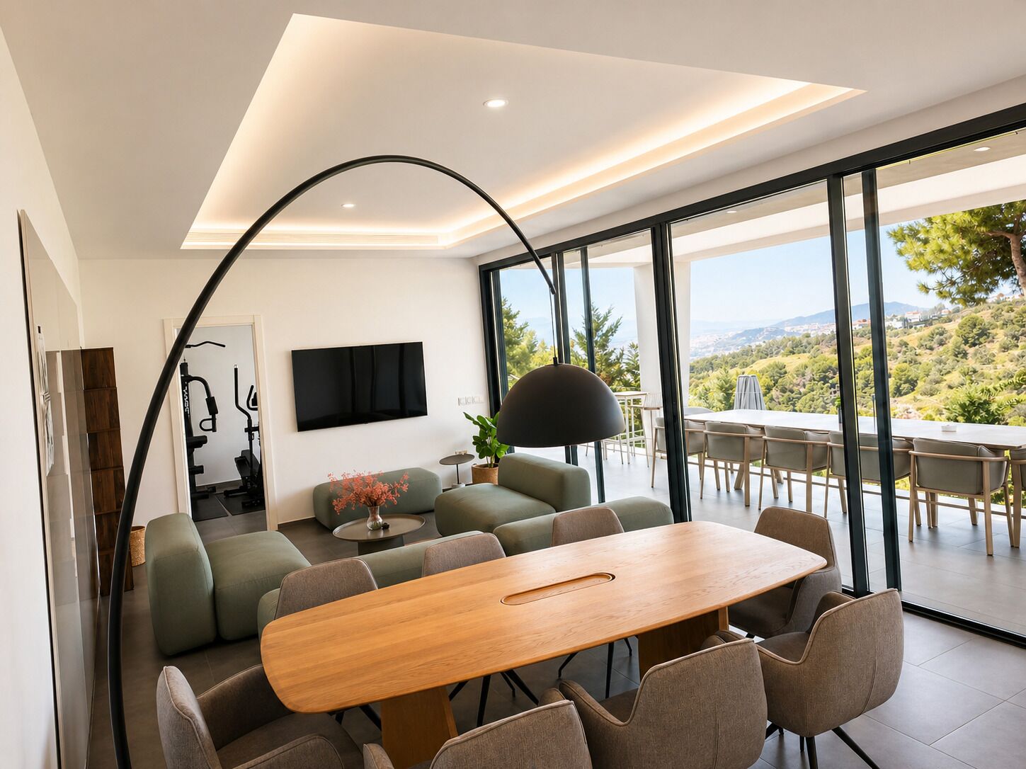 A modern interior with a dining area, sofa, TV, and large windows offering a scenic view.