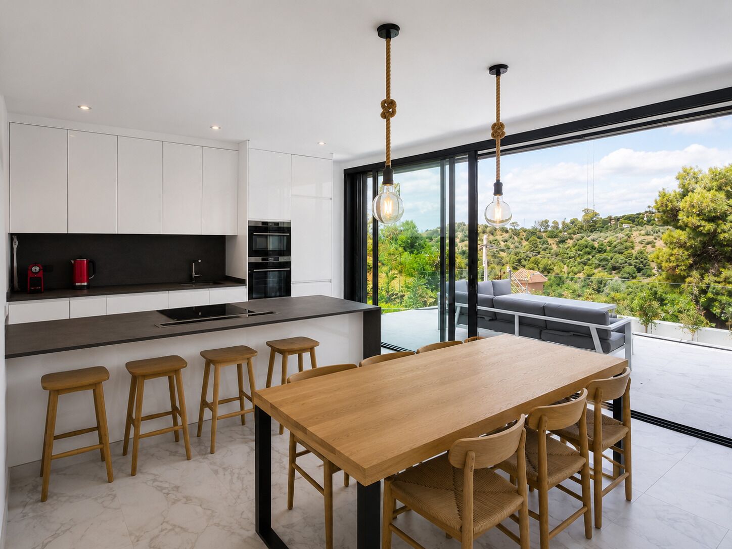 Una cocina moderna con armarios blancos, encimera negra y una mesa de comedor de madera con cuatro taburetes.