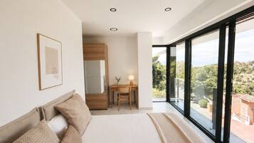 A bedroom with a large bed, a desk, and a view of the outdoors.