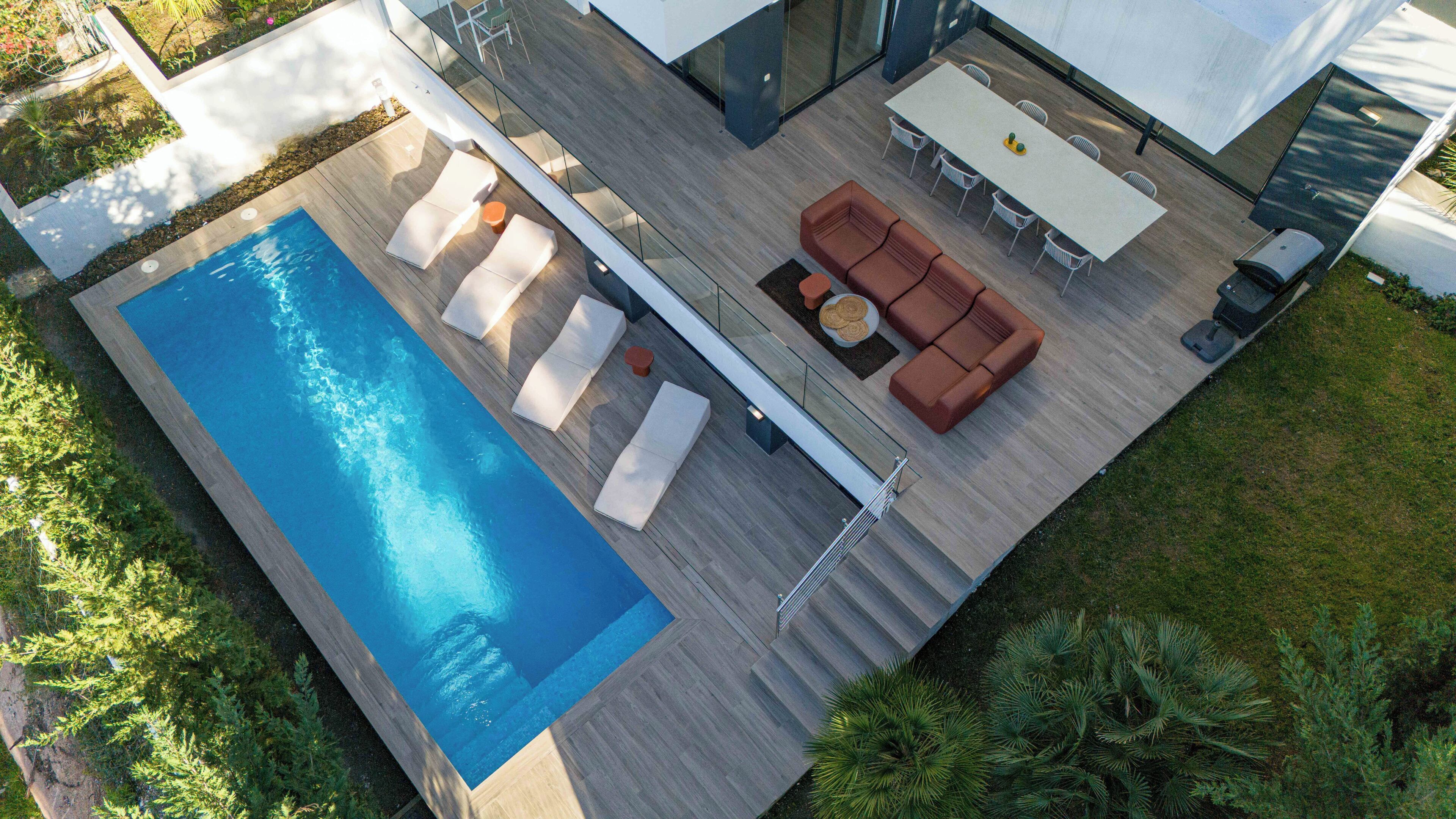 A modern outdoor pool area with lounge chairs, a dining table, and a sofa.