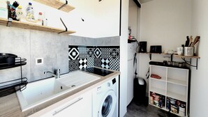 A compact kitchen with a washing machine, a sink, and shelves with various kitchen items. - Renovated seafront studio in Canet, near amenities, ideal for 3 people (Canet-en-Roussillon)