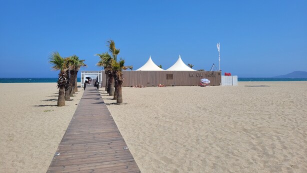 A beach with a wooden walkway leading to a white tented structure labeled "LA NYL VAGUE". - Renovated seafront studio in Canet, near amenities, ideal for 3 people (Canet-en-Roussillon)