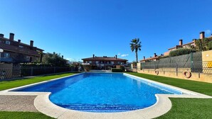 A swimming pool with a clear blue water, surrounded by a well-maintained lawn and a fence.