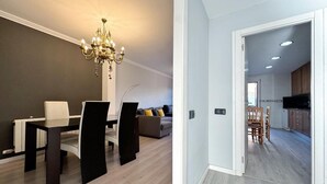 A modern dining area with a chandelier, a sofa, and a kitchen visible through an open door.