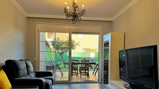 A living room with a sofa, a TV, and a sliding glass door leading to an outdoor area with a table and chairs.