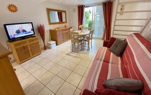 Un salon comprenant un téléviseur, une table à manger avec des chaises, un canapé et un petit meuble.