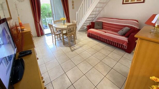 A living room with a red sofa, a dining table with chairs, a TV, and a staircase. - Air-conditioned pavilion with pool, near beach, 2 bedrooms (Valras-Plage)