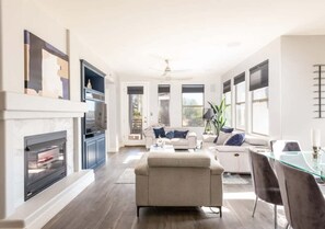 Un salon moderne avec une cheminée, un ensemble de canapés, une table à manger en verre et un ventilateur de plafond.