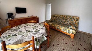 A room with a dining table, a sofa, a television, and a coffee machine.