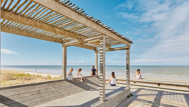 A wooden deck with a pergola overlooking a beach.