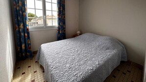 A bedroom with a single bed, a window with curtains, a hanging light fixture, and a tiled floor.
