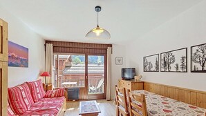 A cozy living room with a sofa, a dining table with chairs, a television, and a view through a large window. - La Clusaz: 31m² Apartment, 4 people, South Balcony (La Clusaz)