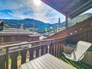 Een balkon met een stoel, met uitzicht op een stad met traditionele gebouwen en een kerktoren.
