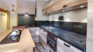 A modern kitchen with wooden cabinets, a black countertop, and stainless steel appliances. - La Clusaz: Studio 4 pers, Balcony, Wifi, Pets allowed (La Clusaz)