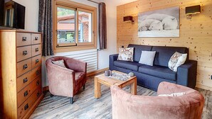 A cozy room with a wooden wall, a sofa, a chair, a wooden table, and a dresser. - La Clusaz: Studio 4 pers, Balcony, Wifi, Pets allowed (La Clusaz)