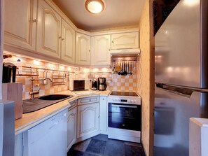 A compact kitchen with white cabinetry, a built-in oven, a microwave, and a stainless steel refrigerator.