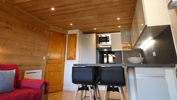 A compact kitchen with wooden ceiling beams, a microwave, and a sink. There are two black chairs and a red sofa in the adjacent living area. - 2-room apartment, 4 pers, 4*, parking, Valloire (Valloire)