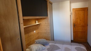 A small, cozy bedroom with a wooden sloped ceiling, a single bed with a patterned quilt, two pillows, and a small shelf with a decorative item. - 2-room apartment, 4 pers, 4*, parking, Valloire (Valloire)